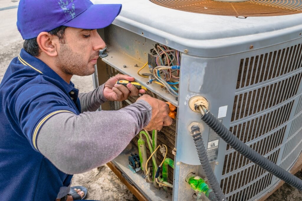 a professional electrician man is fixing the heavy unit of an air conditioner at the roof top of a building and wearing blue uniform and head cap