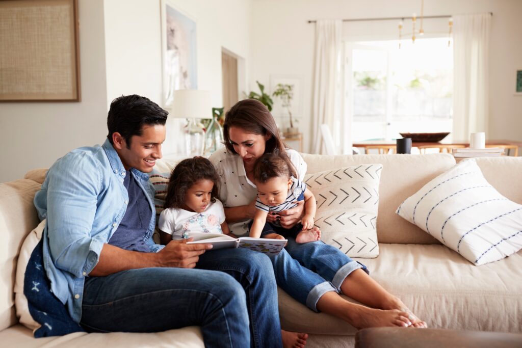 couple sitting on the sofa reading a book at home with their baby son and young daughter
