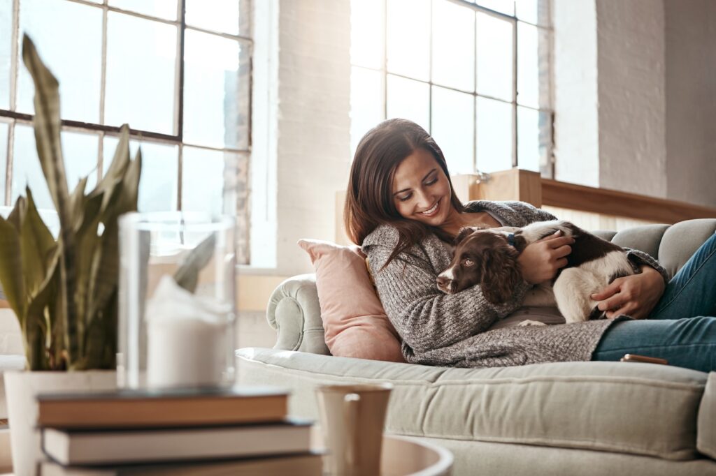 Woman relax on couch with puppy, happy and content at home with pet, happiness together with peace in living room. .Female cuddle dog, love for animals with smile and care, stress relief and comfort.