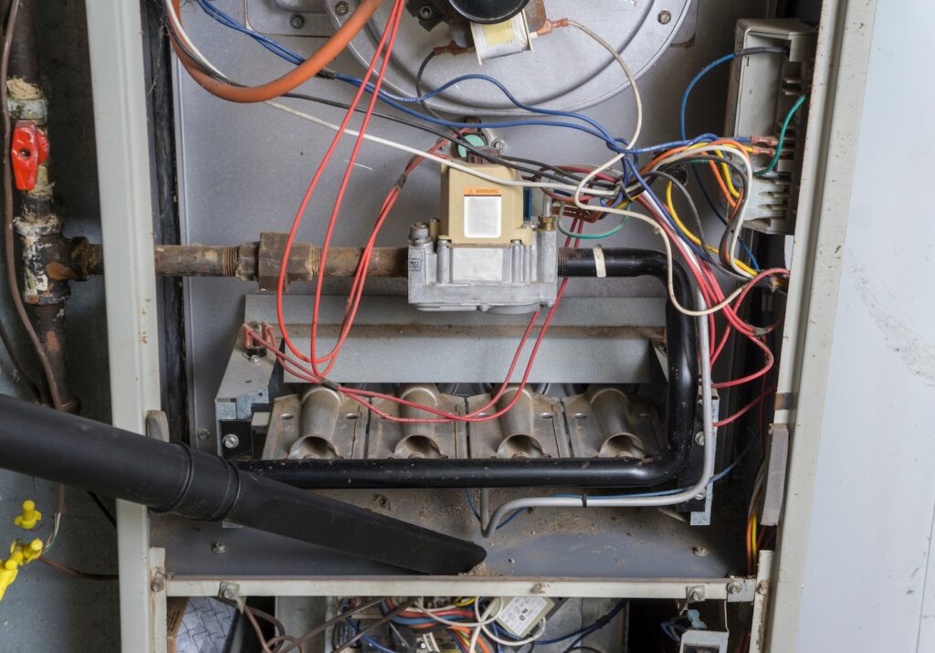 Repairman vacuuming inside of a gas furnace during a cleaning.