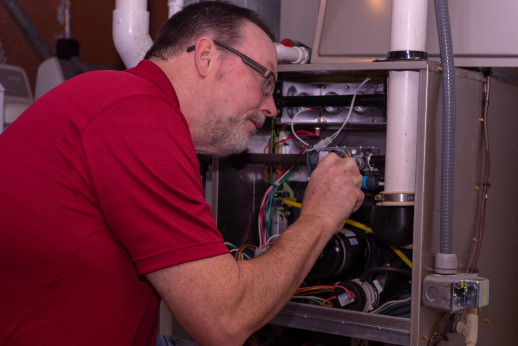 HVAC Tech Making A Repair To Furnace Red Shirt