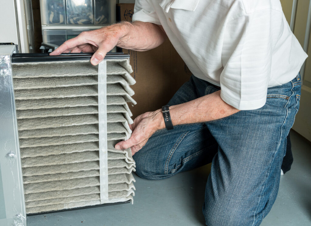 Senior man changing a folded dirty air filter in the HVAC furnace system in basement of home