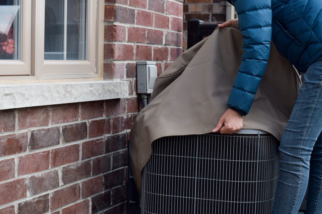Woman putting cover on air conditioner unit outside the house