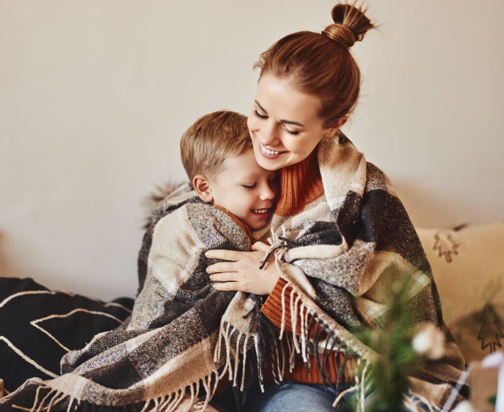 happy family mother and loving son hug and laugh wrapped in a warm blanket on a cozy winter evening at home