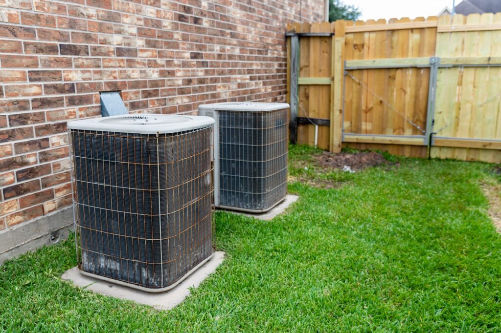 Two older HVAC air conditioner systems next to brick home with copy space.