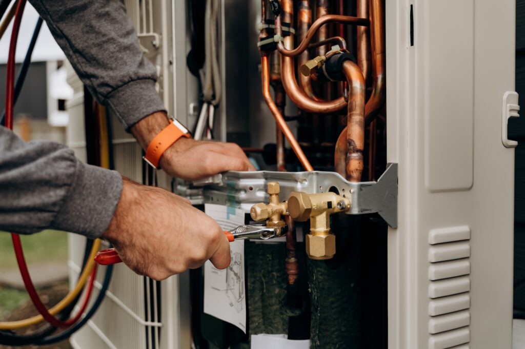 Technician's hands with tools working on the copper pipes of the air conditioner. The photo shows parts of the cooling system and connecting valves.