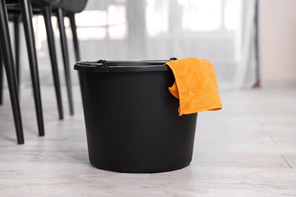 Black plastic water bucket with orange cloth rag. 
