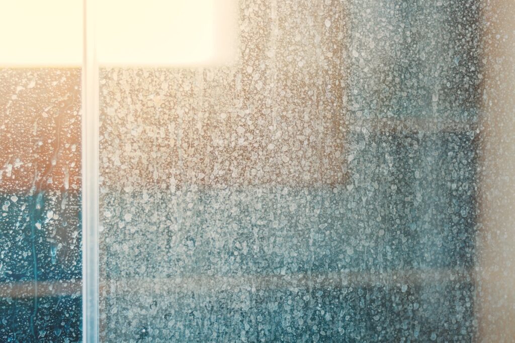 Hard water stains on a glass shower door indicating the need for water softener installation.