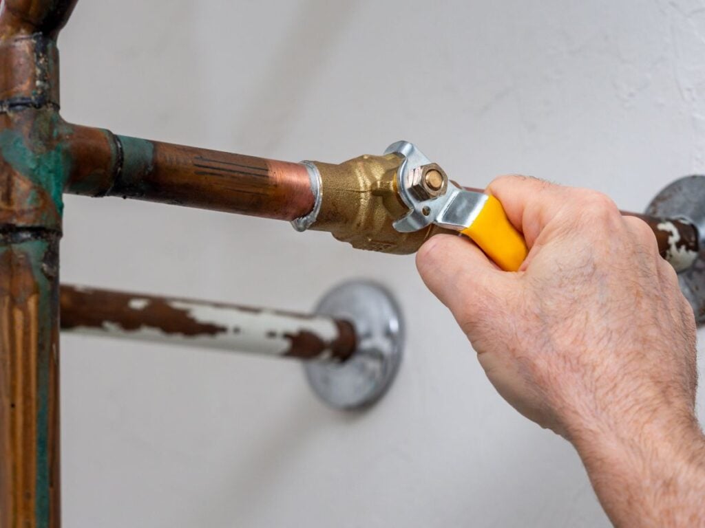 Plumbing man turning off water valve inside modern house