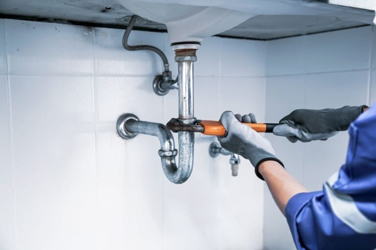 Plumbing worker with blue clothes and grey gloves fixing water pipe using wrench