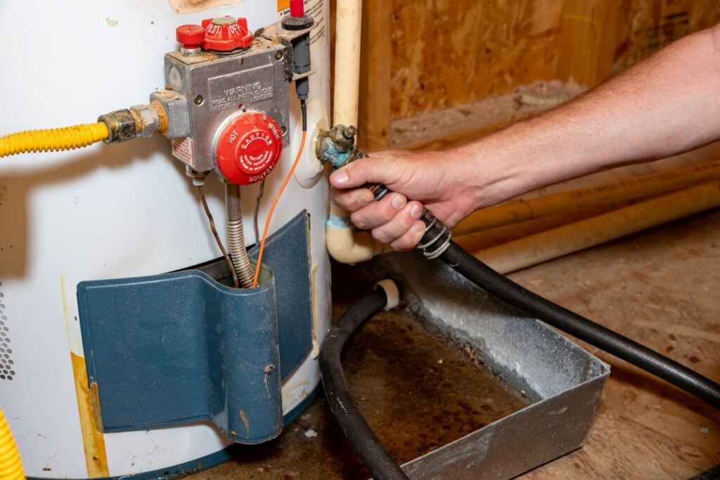 Water Heater hand using hose to drain water from old heater