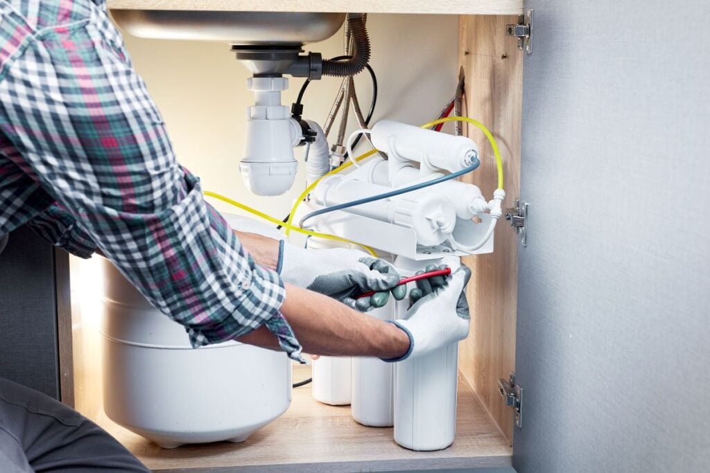 Water Quality Technician installing system of water filtration using white gloves inside modern house
