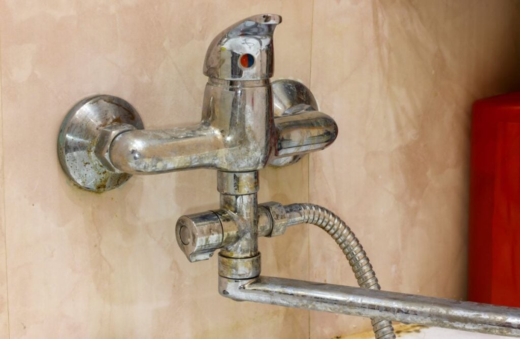 Water Quality old faucet corrored by limescale buildup on beige tiled wall inside bathroom