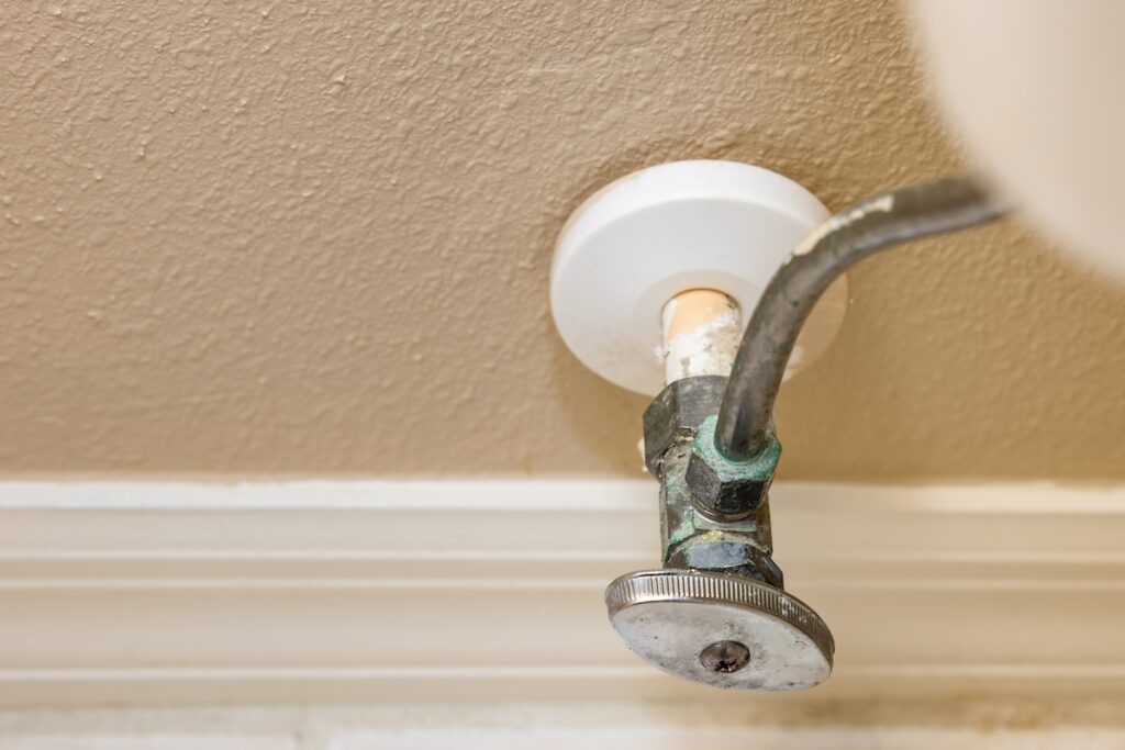 Residential home bathroom toilet water shut off valve. Replacing old leaking restroom wall supply line valve plumbing.