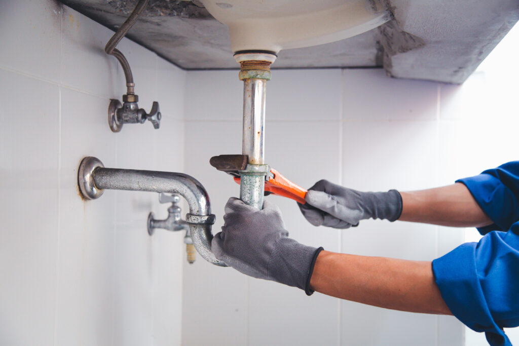 Technician plumber using a wrench to repair a water pipe under the sink.